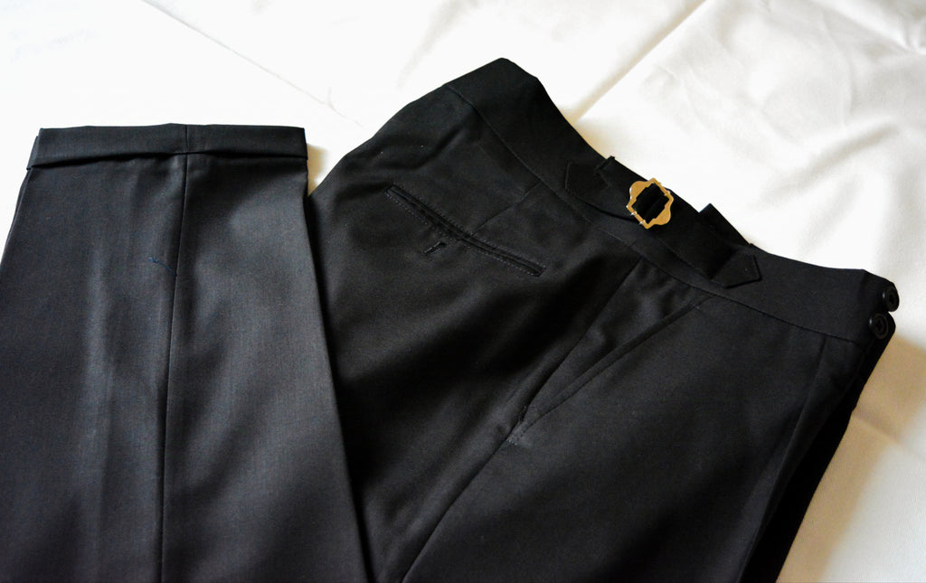 Close-up of black pleated trousers showing fabric texture, stitching, and premium tailoring finish
