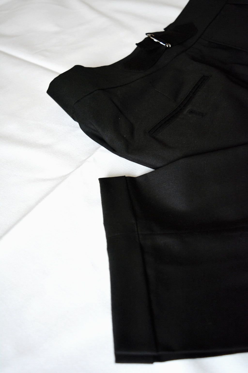 Black men’s pleated trousers fabric texture with folded hem and refined tailoring detail