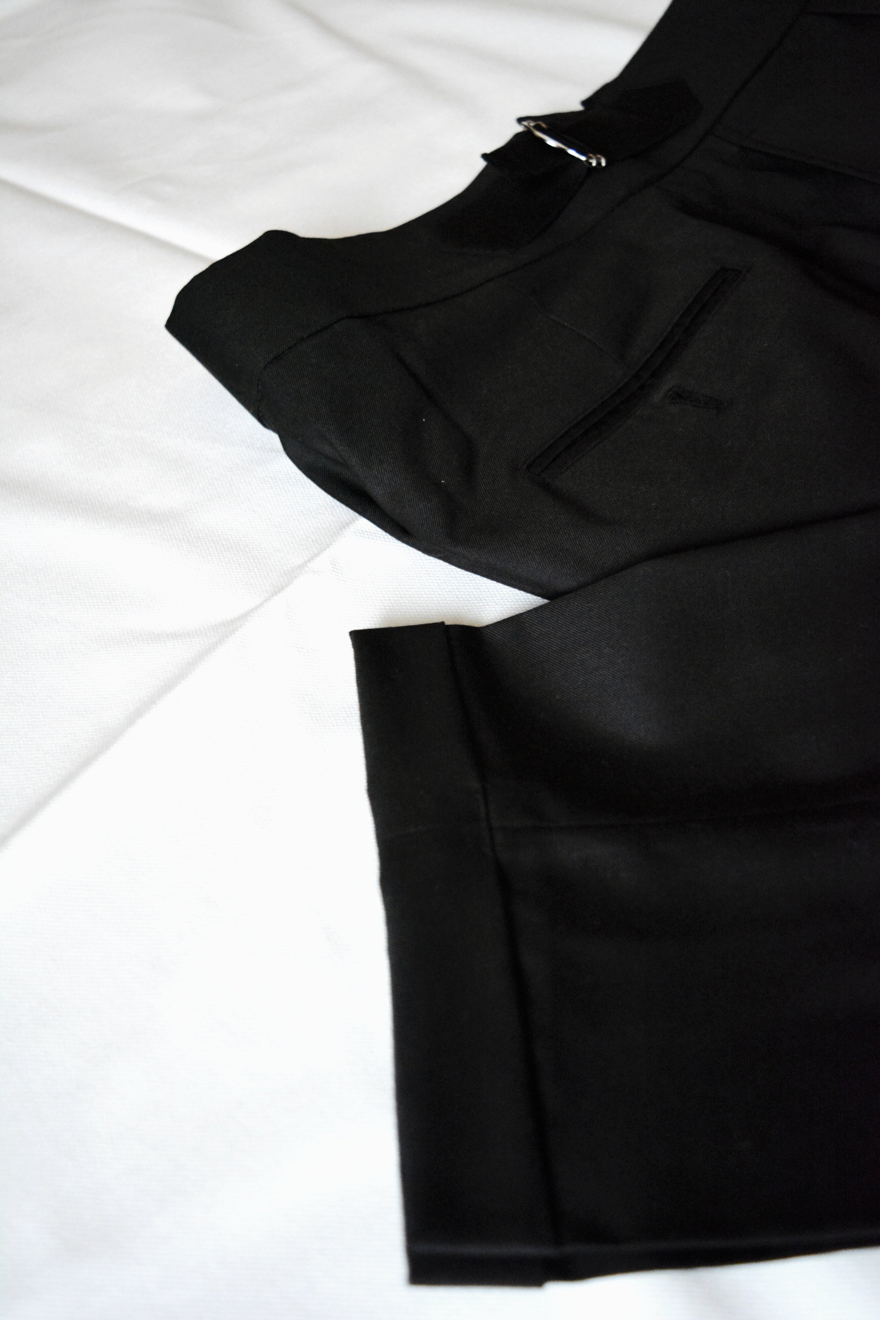 Black men’s pleated trousers fabric texture with folded hem and refined tailoring detail