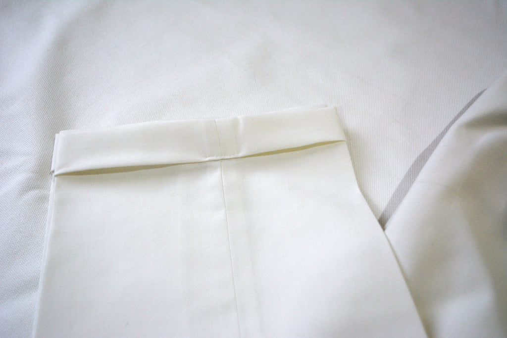 Off-white men’s pleated trousers fabric texture with folded hem and refined tailoring detail
