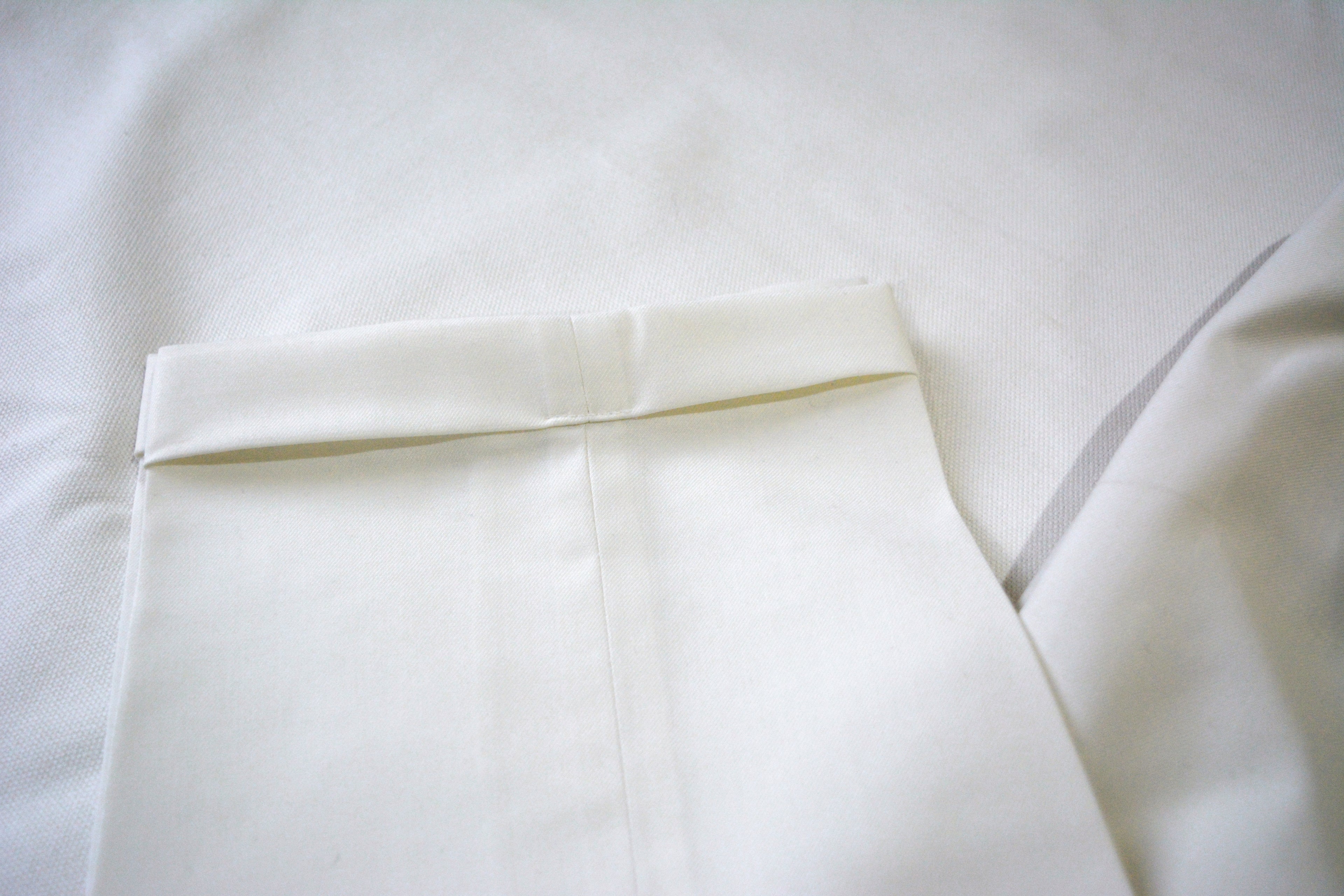 Off-white men’s pleated trousers fabric texture with folded hem and refined tailoring detail
