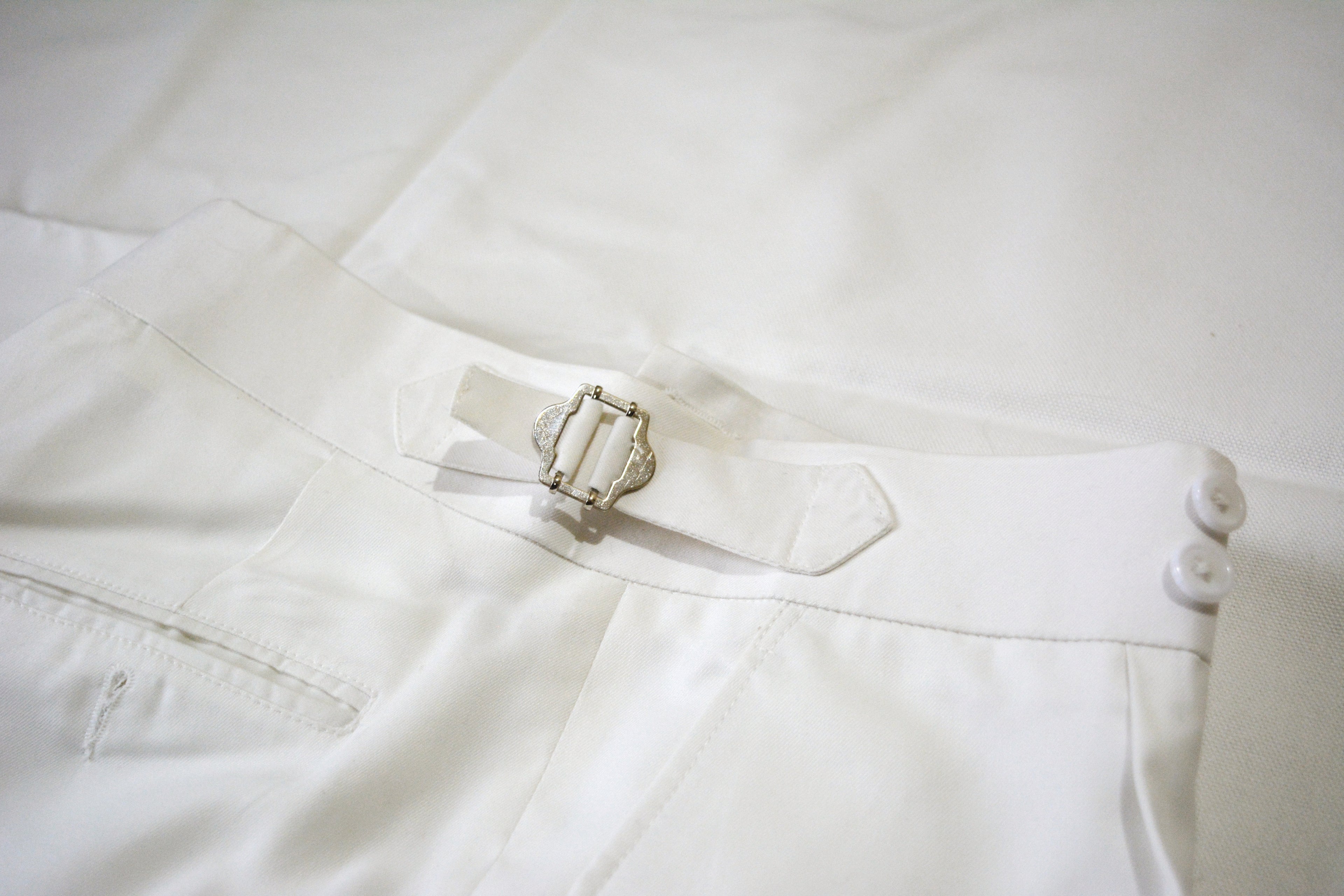 Men’s off-white tailored pleated trousers with adjustable side buckles and double waist button closure